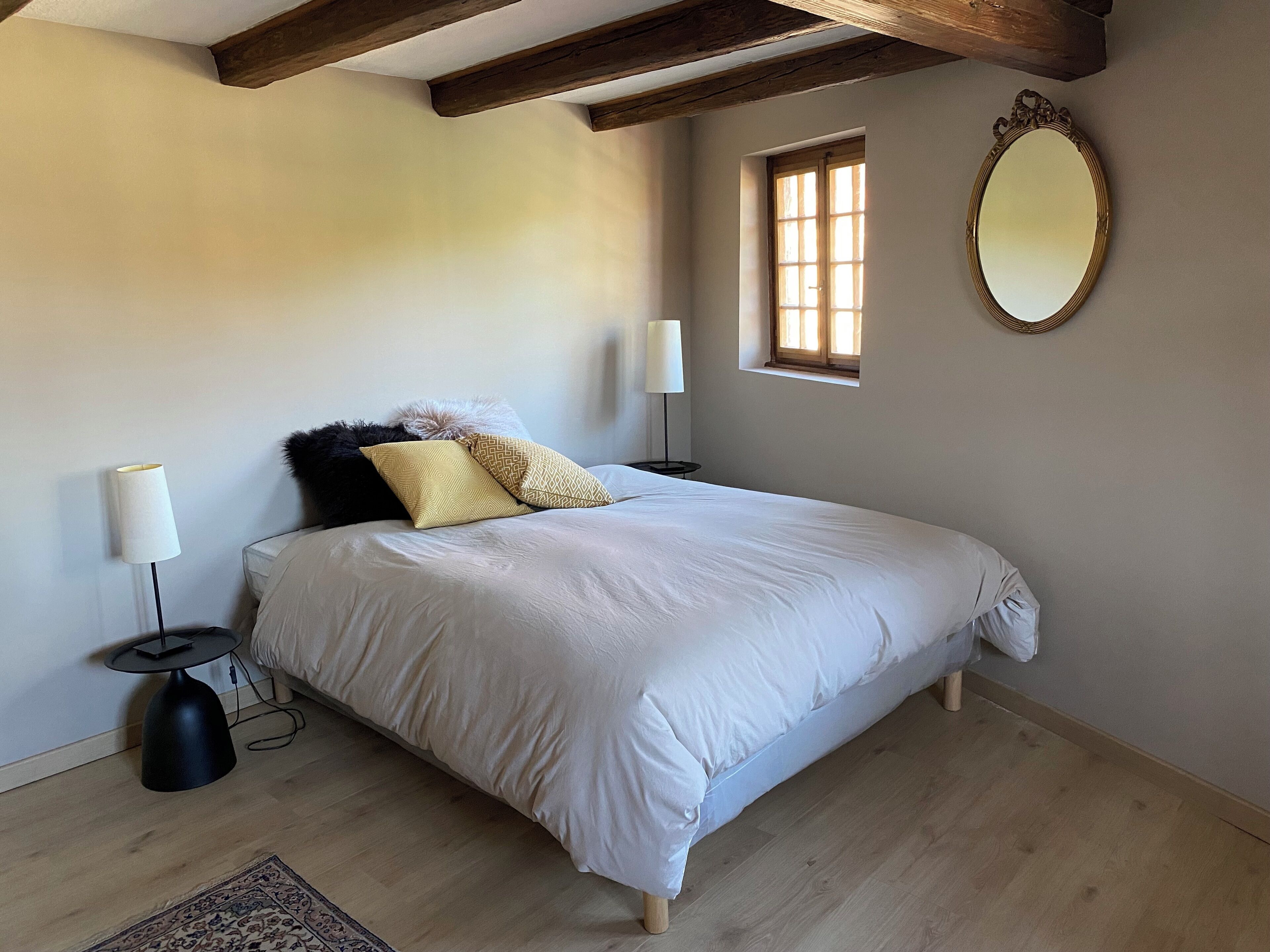 Un dormitorio con una cama grande, dos lámparas de noche, una ventana con vistas y un espejo en la pared.