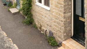 Un bâtiment en pierre avec une entrée étroite, une porte bleue et un petit marchepied menant à l’entrée.