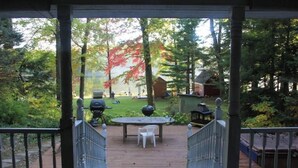 Une terrasse en bois avec une table et des chaises, entourée d’arbres et d’une pelouse.