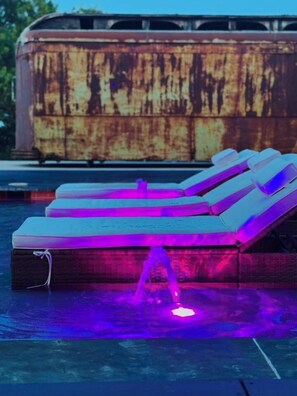 A poolside lounge area with a large, rusted structure in the background.