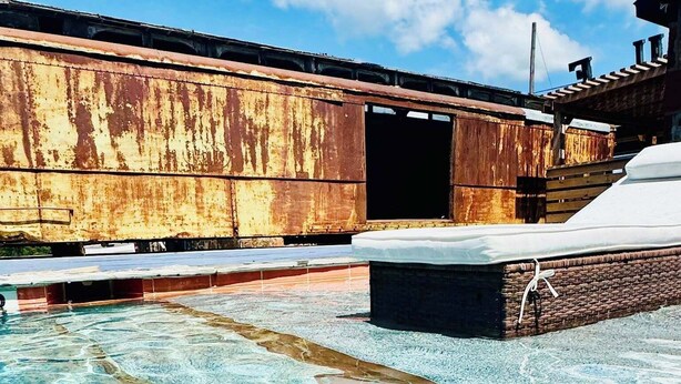 A pool with a clear water feature, a wooden deck, and a rusted metal wall in the background. - Lone Ranger RV Park & Lodge (Ranger)