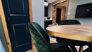 A dining area with a round table, green upholstered chairs, and a dark blue door. - Lone Ranger RV Park & Lodge (Ranger)