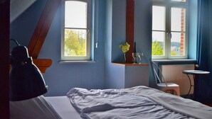 A bedroom with a bed, a chair, a table, and two windows. - Complete guesthouse on the Finow Canal (former school from 1875) for 12 people (Wandlitz)