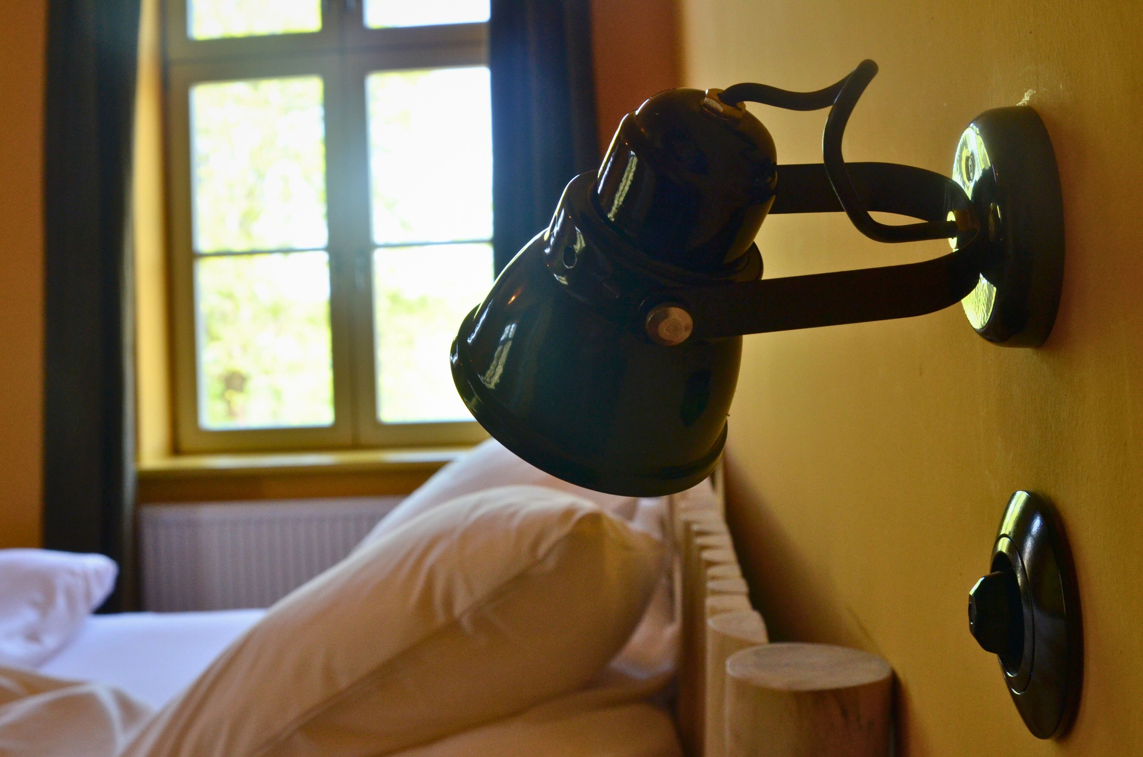 A wall-mounted lamp in a room with a window, a bed, and a radiator.