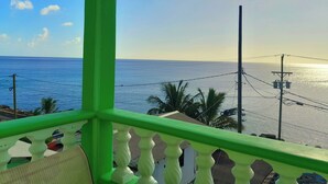 Un balcón con baranda verde que da a una playa con palmeras y cielo despejado.