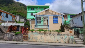 Una casa de dos pisos con un piso superior verde y un piso inferior color beige, que cuenta con un porche pequeño y una escalera visible.