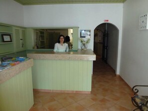 A reception area with a light green counter, a tiled floor, and a framed sign on the wall. - Alojamentos Turísticos Mira-parque (Albufeira)