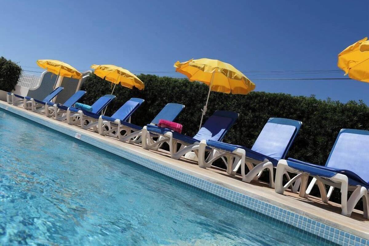 Uma área na beira da piscina com espreguiçadeiras e guarda-sóis amarelos.