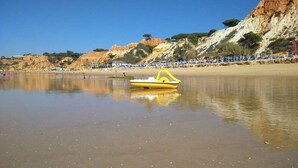 Una playa con un bote amarillo, agua tranquila y un acantilado rocoso al fondo.