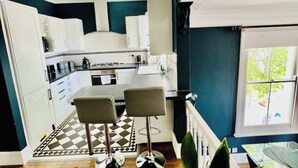 A kitchen with white cabinets, a black and white checkered floor, and two bar stools. - Richmond charm cozy apartment (Richmond)