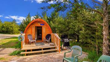 A cozy, wooden A-frame cabin with a porch, two chairs, a grill, and a sign reading "The Nook".