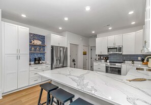 A modern kitchen with white cabinetry, a marble island, and stainless steel appliances. - 300 steps to beach~Private Pool~Elevator~Games~NewHome (Surfside Beach)