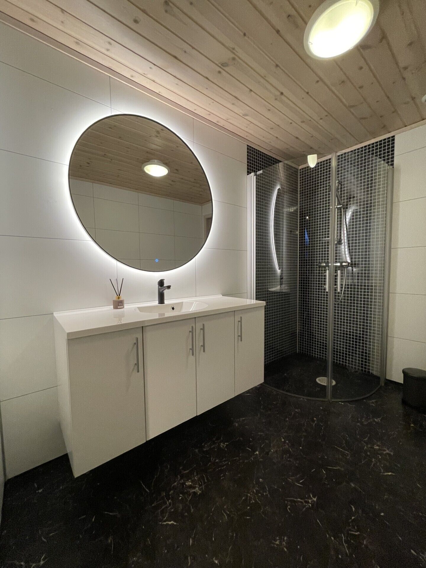A modern bathroom with a round mirror, a white vanity, and a glass-enclosed shower.