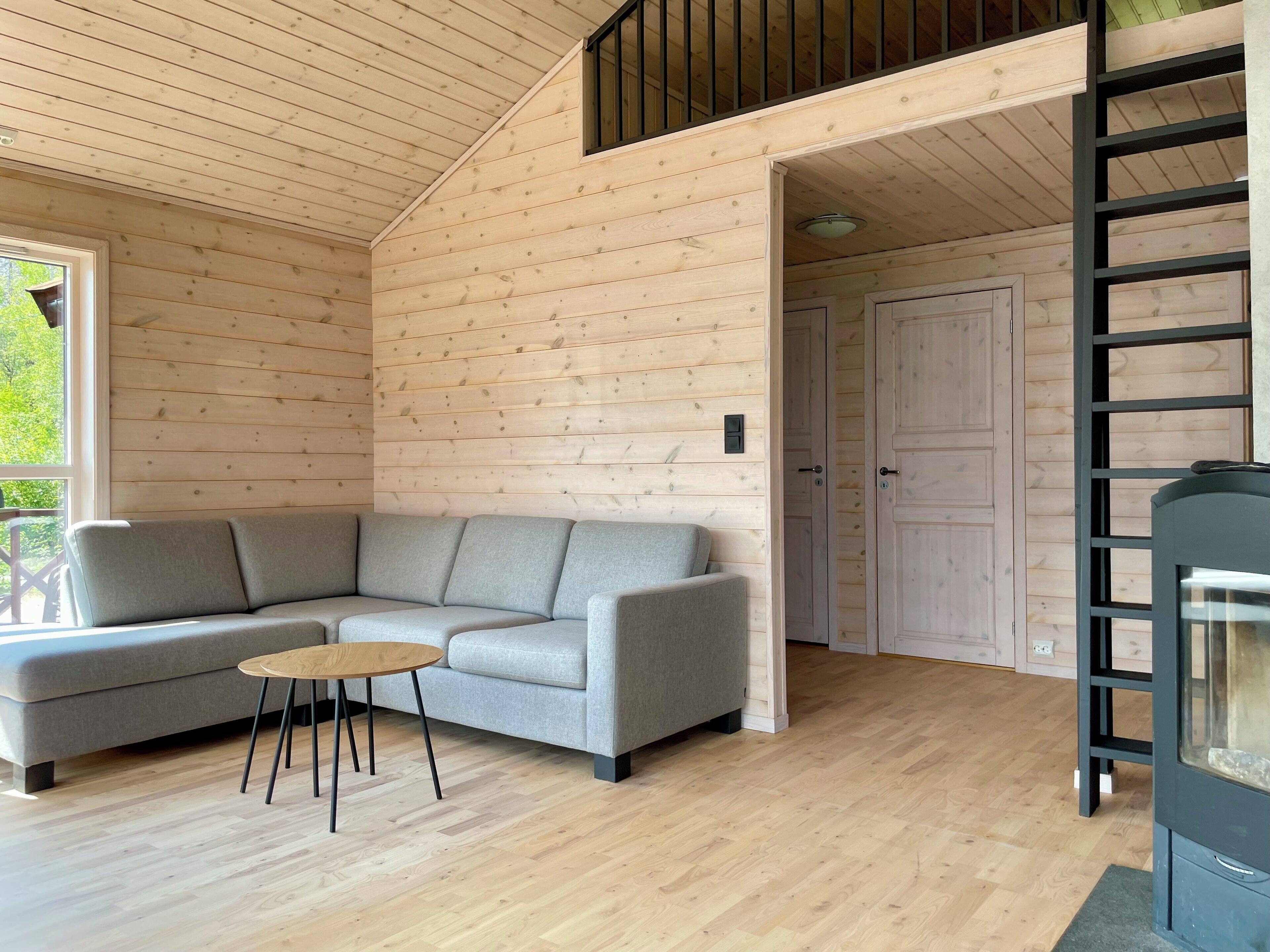 A modern log cabin interior with a grey sofa, a small round table, and a black ladder.