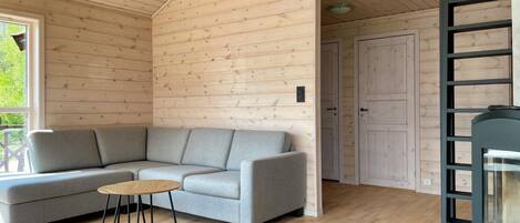 A modern log cabin interior with a grey sofa, a small round table, and a black ladder.