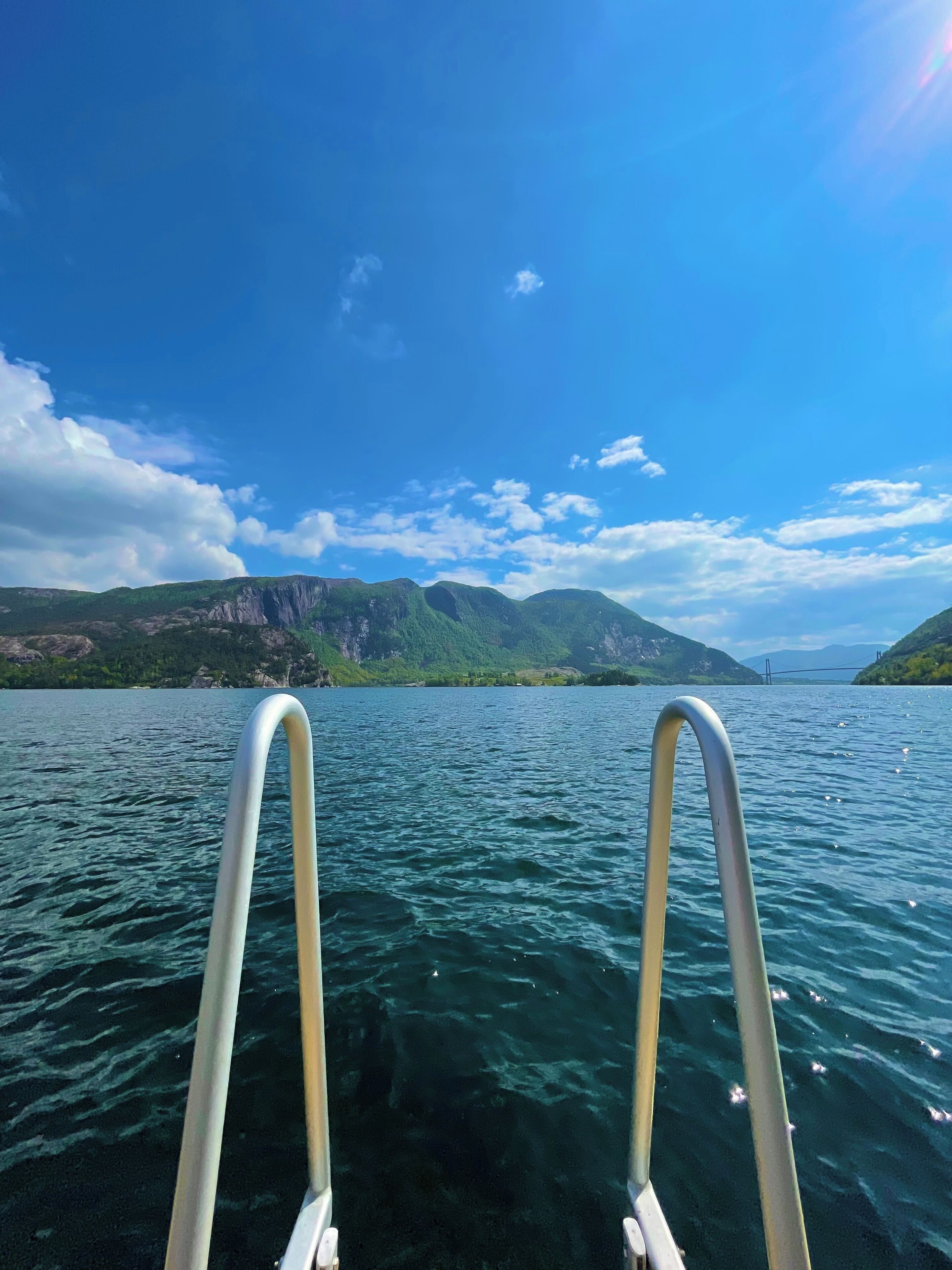 A view from a boat with metal railings, a calm lake, and mountains in the background.