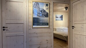 A wooden cabin interior with a bed, a poster of a mountain landscape, and a door leading to another room. - FjordCabin Preikestolen (Rogaland)