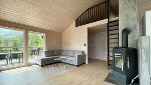 A modern log cabin interior with a gray sectional sofa, a small round table, and a wood-burning stove. - FjordCabin Preikestolen (Rogaland)
