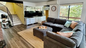 Ein modernes Wohnzimmer mit einem Ecksofa, einem Flachbildfernseher, einer Treppe und einem großen Fenster.