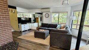 Ein modernes Wohnzimmer mit einem Ecksofa, einem Fernseher und einem großen Fenster.