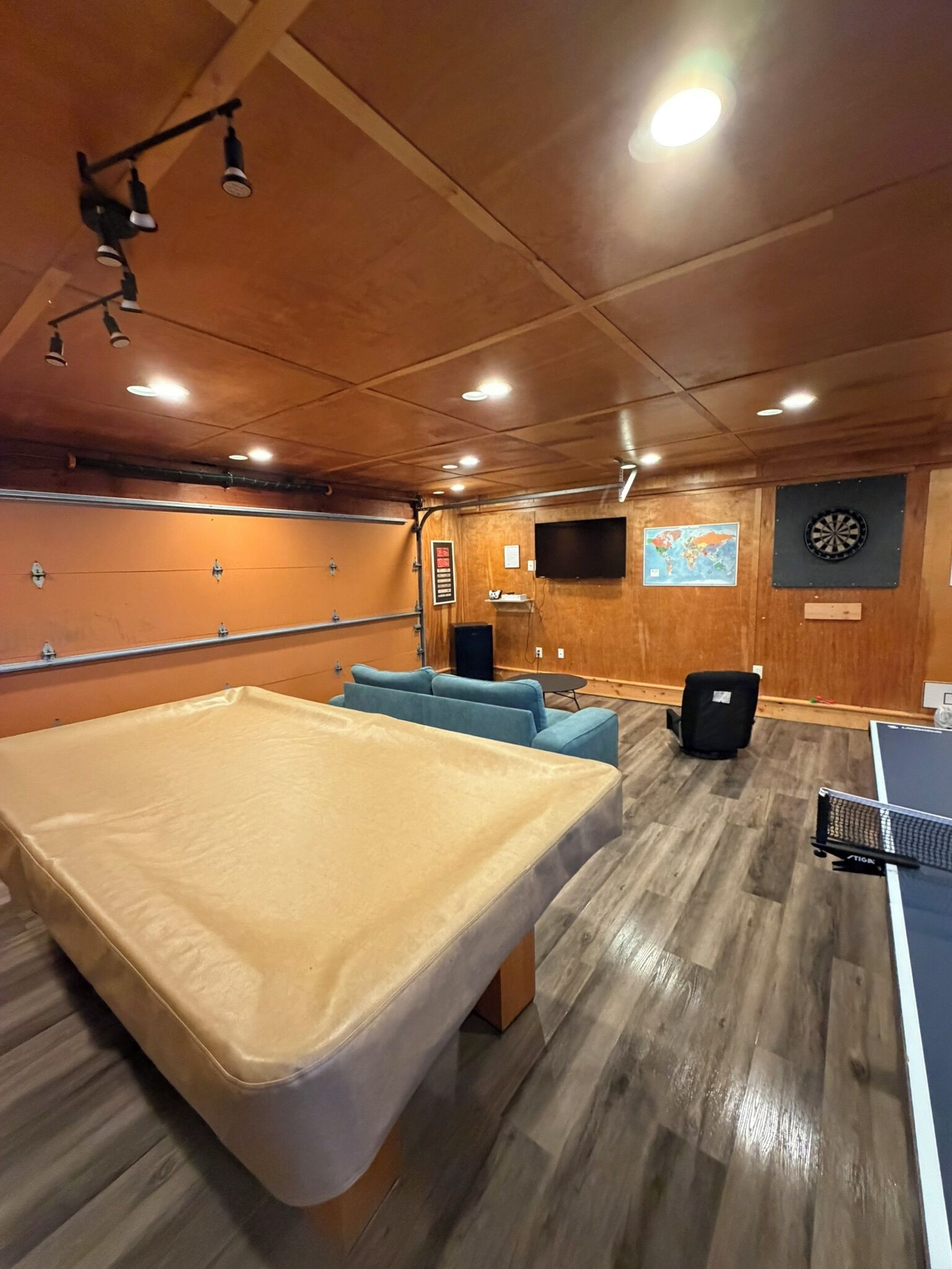 Ein Zimmer mit einem großen Bett, einer Dartscheibe, einem an der Wand montierten Fernseher und einer weiteren Dartscheibe auf der gegenüberliegenden Wand.