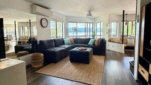 Ein geräumiges Wohnzimmer mit einer Eckcouch, einem Couchtisch und einem großen Fenster mit Blick ins Freie.