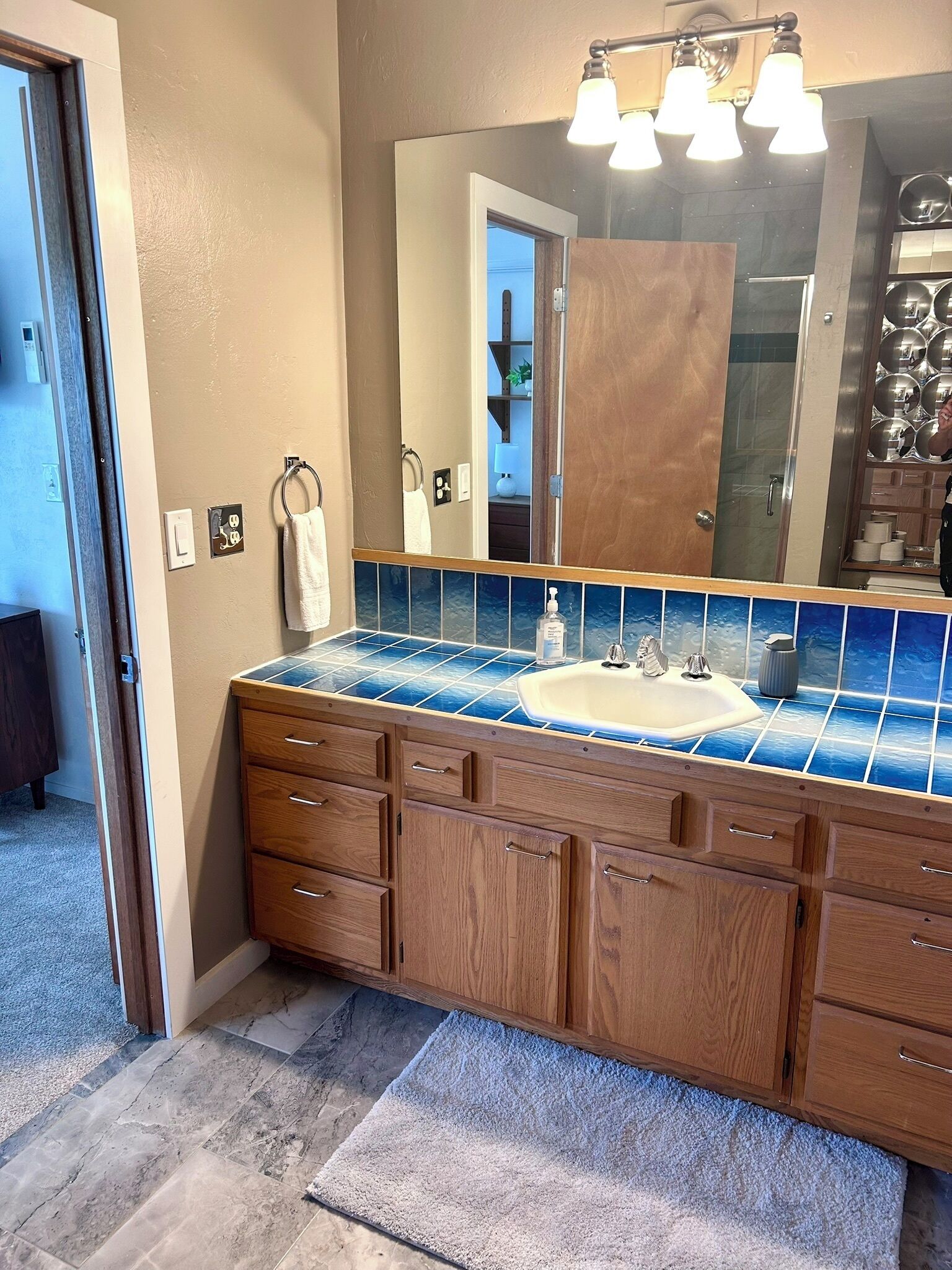 Ein Badezimmer mit einem Holz-Waschtisch, einem großen Spiegel und einer blauen Fliesenrückwand.