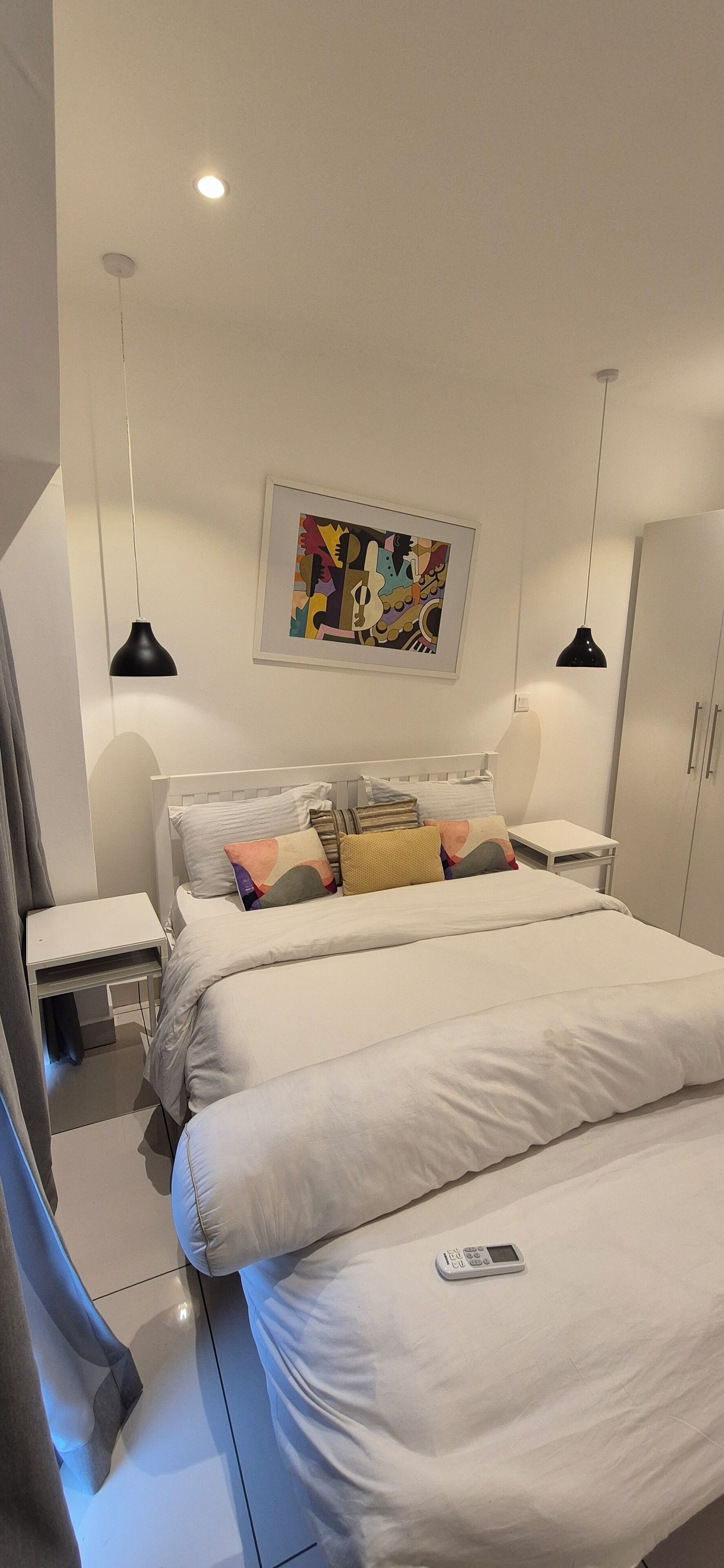 Une chambre à coucher moderne avec un grand lit, des tables de chevet, une commode, une armoire et un tableau abstrait aux couleurs vives accroché au mur.