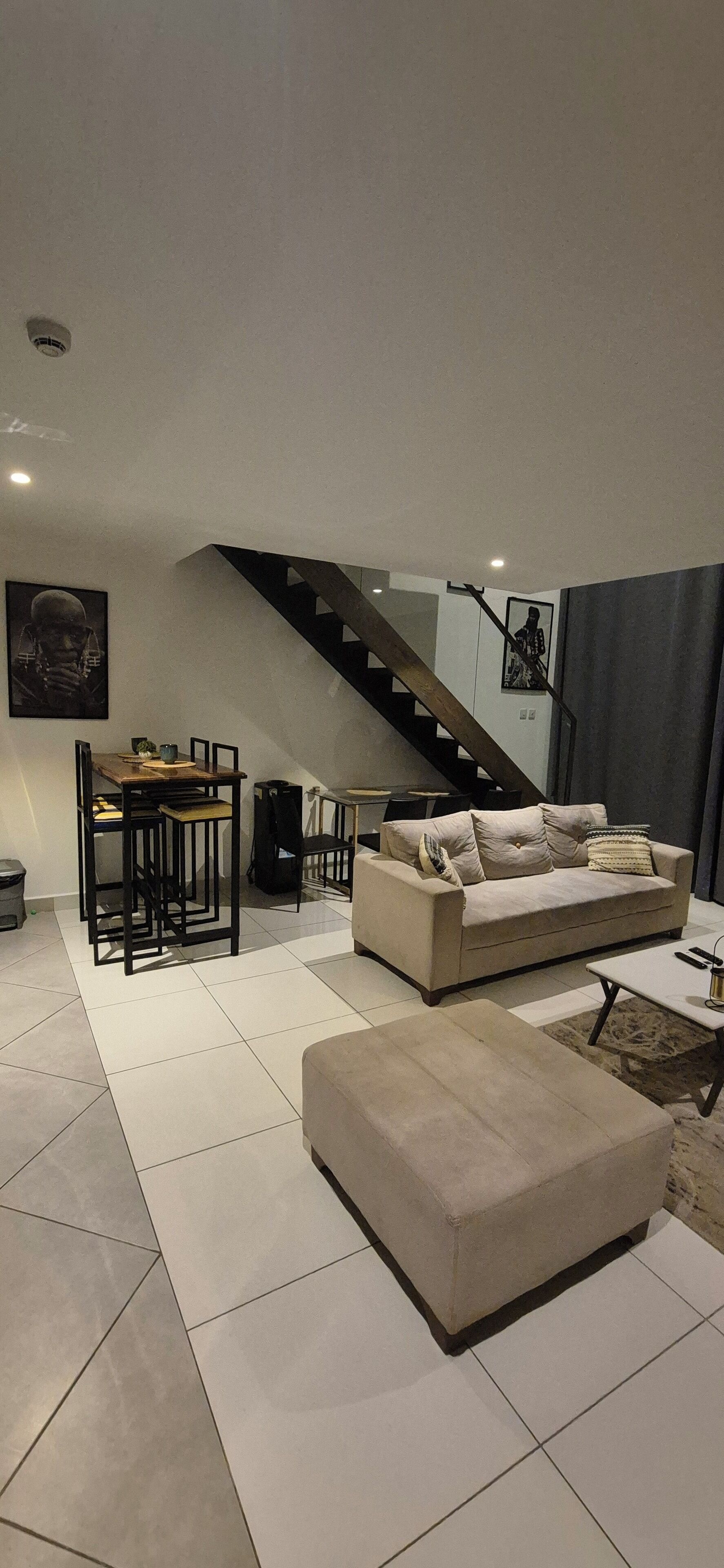 Ein modernes Wohnzimmer mit einer Couch, Hocker und einem Essbereich mit Stühlen und Tisch.