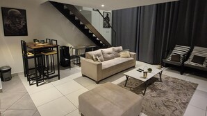 A modern living room with a sofa, coffee table, and a staircase leading to another level. - premier luxury apartment (Accra)