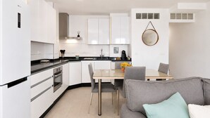 A modern kitchen with white cabinets, a dining area with a table and chairs, and a grey sofa with a light blue pillow. - Comeback El Mar Ciega tus Ojos (Torrenueva)