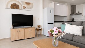 A modern living room with a flat-screen TV, wooden cabinets, a grey sofa, and a small table with a vase of flowers. - Comeback El Mar Ciega tus Ojos (Torrenueva)