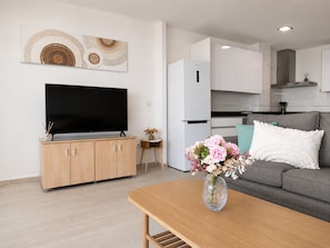 A modern living room with a flat-screen TV, wooden cabinets, a grey sofa, and a small table with a vase of flowers.