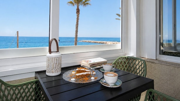 A table with a cake, two cups of coffee, and a book by a window overlooking the sea. - Comeback El Mar Ciega tus Ojos (Torrenueva)