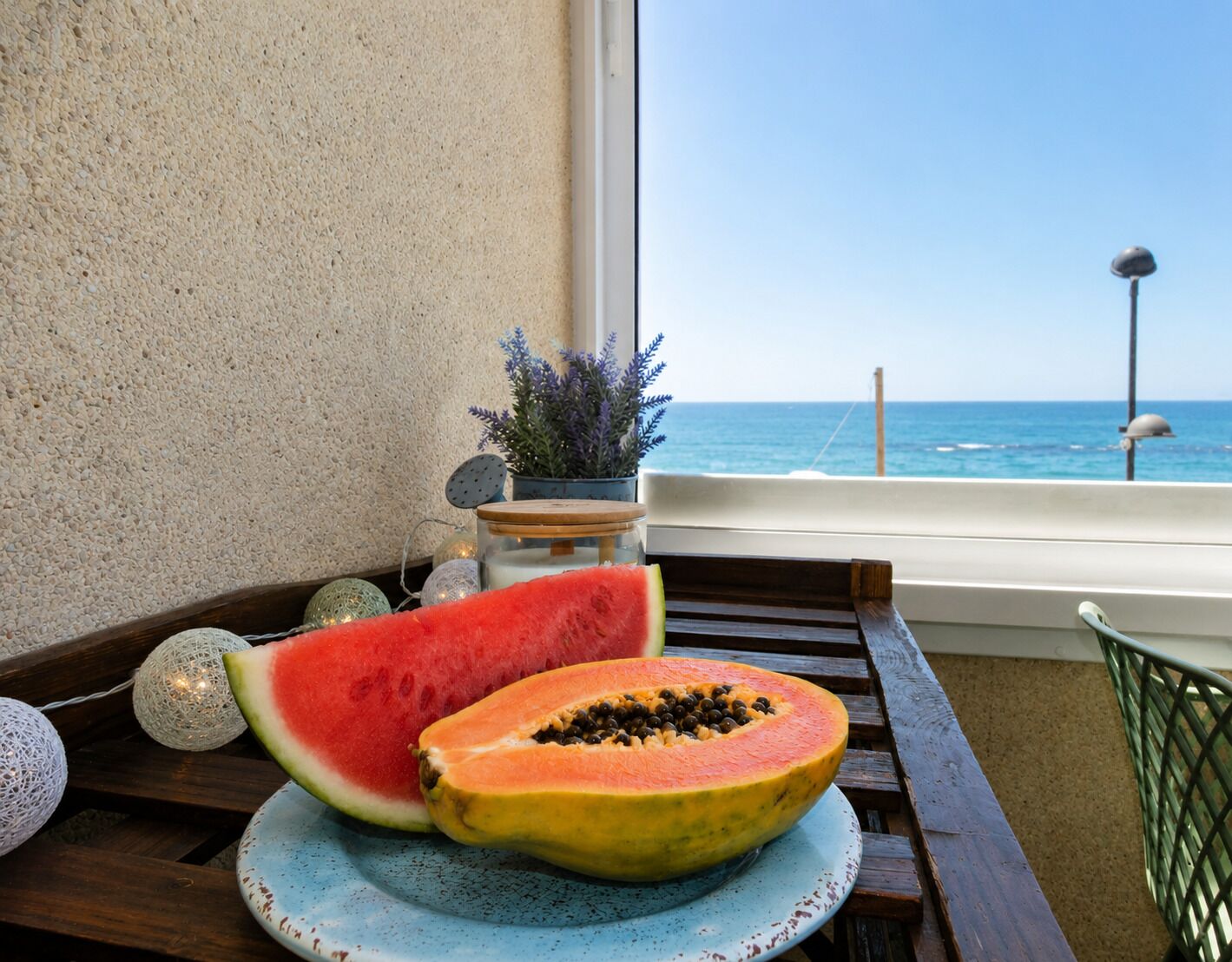 A wooden table with a blue plate holding a halved watermelon and a halved papaya, a potted plant, and decorative lights.