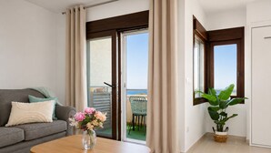 A room with a sofa, a table with a vase of flowers, a potted plant, and a view of the sea through a sliding door. - Comeback El Mar Ciega tus Ojos (Torrenueva)
