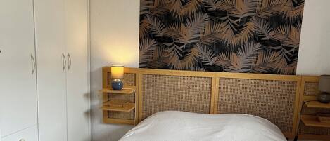 A bedroom with a bed, a wardrobe, a bedside table with a lamp, and a wall with a leaf pattern.