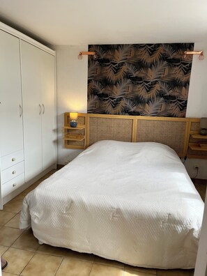 A bedroom with a bed, a wardrobe, a bedside table with a lamp, and a wall with a leaf pattern.