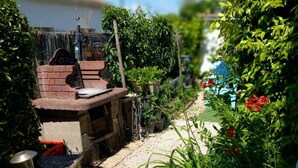 Un jardin avec un espace barbecue, des plantes en pot et un sentier.