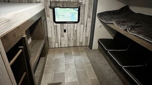 A compact room with a bunk bed, a small window with a view, and a tiled floor. - Up North in Comfort – Your Dream Camper Getaway! (Roscommon)