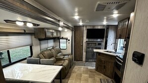 A compact RV interior with a dining area, a seating area, and a kitchenette. - Up North in Comfort – Your Dream Camper Getaway! (Roscommon)