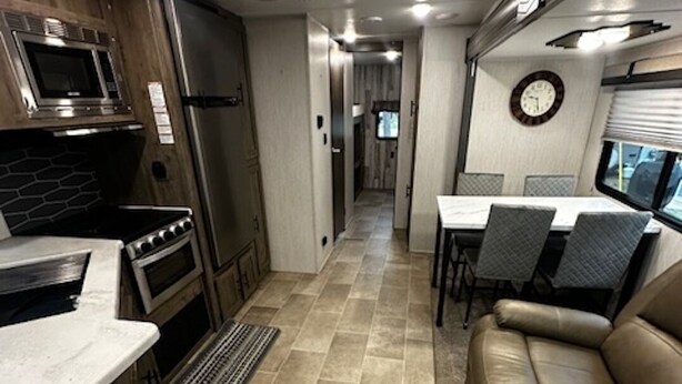 A compact RV interior with a kitchenette, dining area, and a seating space. - Up North in Comfort – Your Dream Camper Getaway! (Roscommon)