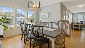 Un espace repas avec une table et des chaises en bois, de grandes fenêtres et un luminaire suspendu.