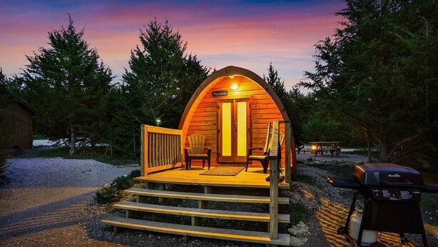 Een knus houten huisje met een veranda, twee stoelen en een barbecue.