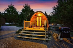 A cozy, wooden cabin with a porch, two chairs, and a grill.