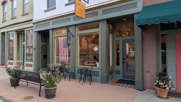 A storefront with a sign reading 'Bailey's Coffee House,' outdoor seating with tables and chairs, and a bench with potted plants.