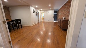 A spacious hallway with wooden flooring, a dining area with chairs, and a brick accent wall.