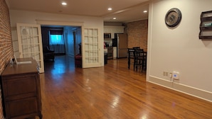 A spacious living area with hardwood flooring, a dining area with chairs, and a kitchen with appliances.