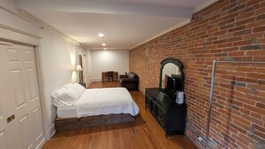 A bedroom with a bed, dresser, mirror, and brick wall.