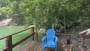 A wooden deck with a blue chair overlooking a green body of water and a rocky shoreline. - Serene cabin with dock/swim platform in charming Speedwell (Speedwell)